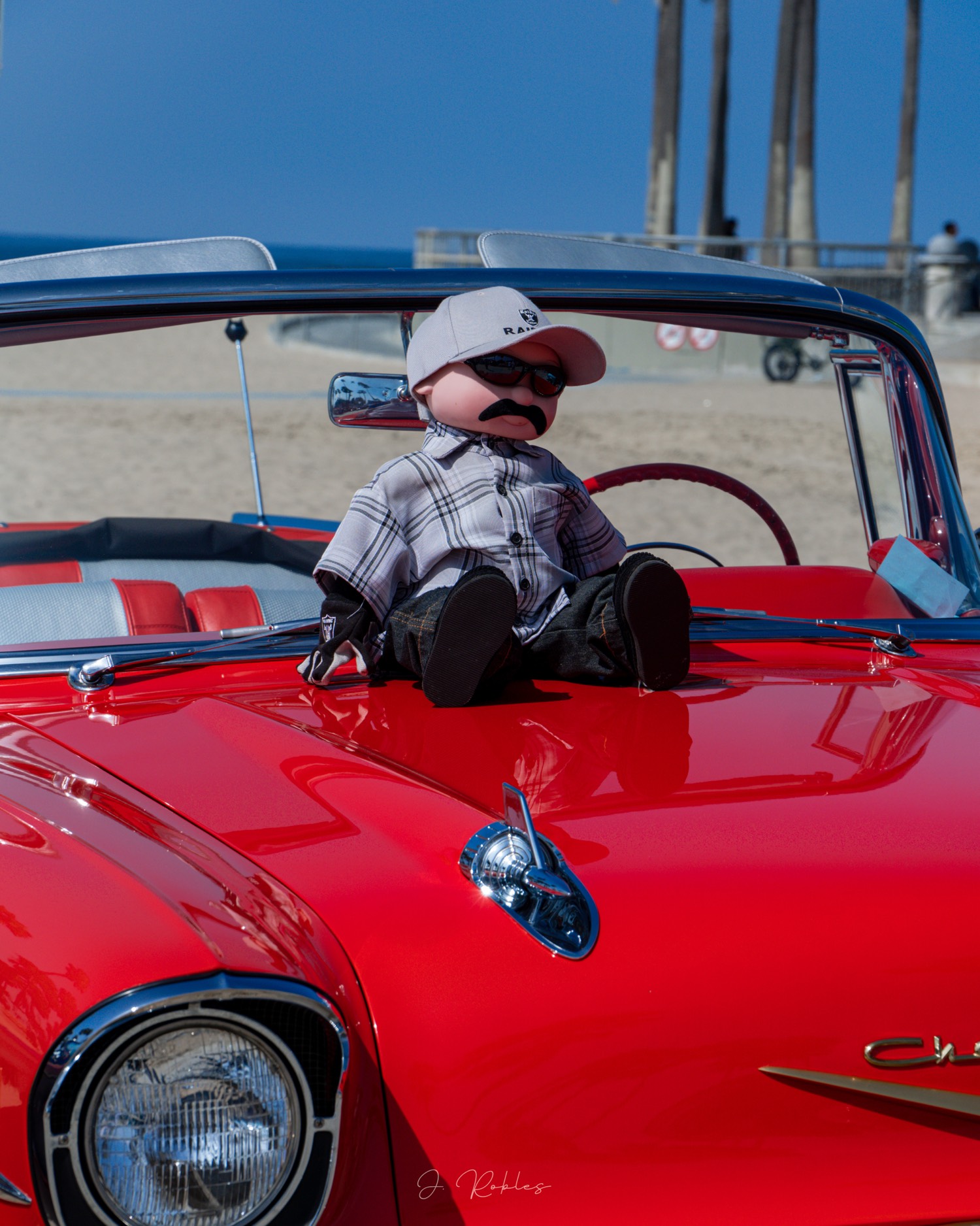 Doll on the hood of a red convertible